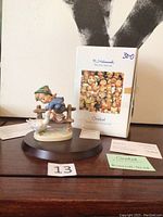 Front view of the figurine alongside original box and documentation, showing figurine on a black display stand.