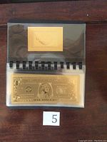 Photo of 1 Dollar gold leaf note in protective sleeve with booklet view
