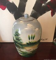 Front view of vase showing painted landscape scene, signed 'Nei 19', and lid.