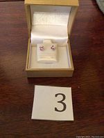 Front view of sterling silver amethyst earrings in tan jewelry box with cream interior, photo includes lot number card 3.
