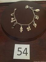 Full view of the sterling silver charm bracelet on a brown circular surface with label "54"