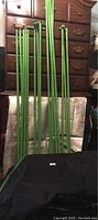 Green metallic poles and folded black fabric with green trim of grow tent visible in front of reflective flooring.