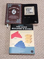 Top view of three books grouped on carpet showing front covers: "Let's Bring Back", "Wreck This Journal", and "The (Unofficial) LEGO Builder's Guide".