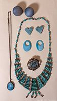 Full view of the 6 costume jewelry items arranged: two pairs of earrings (round wooden buttons, ceramic hearts, pearlescent ovals), a bib-style turquoise bead necklace, curb chain necklace with stone pendant, and a gold-toned flower-like pin with turquoise center.