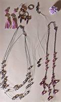 All seven items in the jewelry lot displayed on a pale background: two pairs of earrings, three necklaces laid out, a pink stretch ring, and a carnation pin.