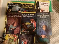 Photo showing eight vintage hardcover Nancy Drew books with colorful illustrated covers mostly intact but worn with age and use.