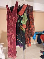 Three dresses on hangers: maroon floral maxi dress, multicolor sleeveless applique dress, black and red ruffled dress.