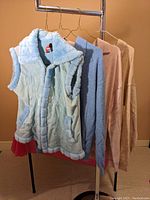Four garments hanging on a clothing rack: three sweaters and one winter fleece vest with faux fur trim.