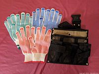Three pairs of gardening gloves with different colored rubber dot grips and a black mesh tool belt laid out on a surface
