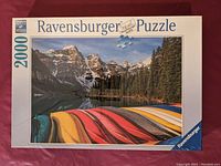 Front view of unopened Ravensburger puzzle box with image of colorful canoes on mountain lake and surrounding forest and mountains.