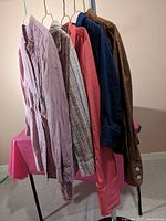 All five button-up blouses hanging on hangers viewed side-on showing colors and fabrics.