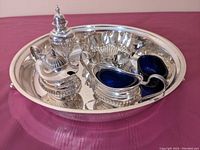 Full view of all silver plate items arranged on the round tray showing salt and pepper shakers, mustard pot with blue liner, candy bowl, and purple glass liner.