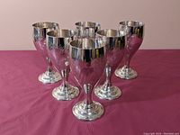Six silver plated goblets arranged in two rows on a purple surface, showing overall set appearance and size.