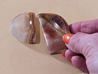 Two brown and white striped polished agate worry stones shown in hand, one semi-circle shaped and the other rectangular with a rounded quarter circle corner.