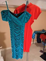 Both dresses hanging on hangers, showing overall length and silhouette. Dark teal green dress in front, bright red dress behind.