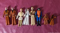 Eight vintage Kenner Star Wars action figures laid out on a red surface showing overall lot contents and condition.