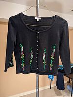Front view of the black acrylic knit cardigan showing floral embroidery and button closure.