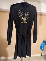 Front view of black acrylic knit dress with long sleeves, high collar, a knit belt, and elephant embroidered on chest in metallic threads.