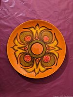 Top-down view of the circular plate showing the full colorful abstract design in orange, green, yellow, and red hues.