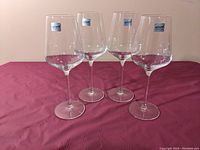 Four clear crystal white wine glasses on a maroon textured surface, each with a Vivo logo sticker on the bowl, displaying height and diameter proportions.