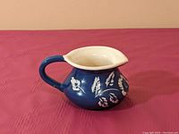 Side angle view showing blue ceramic jug with white floral designs, handle, and spout