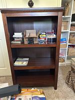 3 shelf wood tone bookcase with items on top shelf and some items on middle shelf