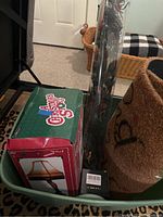 Three boxed or packaged items including the boxed leg lamp replica, a coir mat rolled, and LED branches wrapped in plastic and placed in a plastic bin.