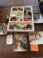Wide view of assortment of costume jewelry pieces in divided white tray and loose on table showing bracelets, earrings, rings, necklaces.