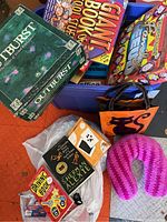 View of board and card games Outburst, Giant Book of Useless Information, Driving Bible card game, Sherman Alexie book, purple neck pillow, and orange tote bag with cat design.