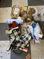 Photo of lot showing plaid ladies rain boots size 10, concrete garden decor statues, glass garden ornament, candle and holder, frame, and various small decorative items in boxes and bags.