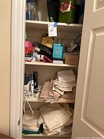Closet shelves with assorted linens folded and stacked, skincare items, toiletry bottles, and boxed items
