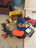 Photo showing various office and workout items on the floor including the back massager box, drawstring bag, pencil case, hole puncher, flashlight, cordless phone base, and sports-themed photo album.