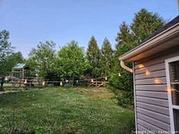 Outdoor light strands hung on the side of a house and across a yard with lawn and trees.