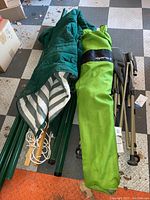 Photo of folded gray tent, green carrying case, hammock fabric, and green metal poles on checkered floor