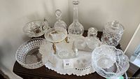 Overview of crystal glass lot on a table including bowls, decanters, small dishes, and jar.