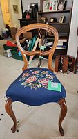 Full view of the wooden dining chair showing carved backrest and blue floral needlepoint seat upholstery.