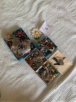 Five small blue boxes containing mixed earrings and brooches, some loose and some in plastic bags, all laid out on a white textured surface.