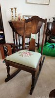 Front view of wooden rocking chair showing carved back and green embroidered seat