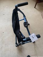 Folded compact walker standing on carpet with black foam handles and mesh middle seat visible.