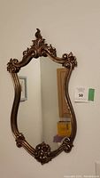 Full view of the metal hanging mirror on a white wall showing the shaped frame with floral decorations.