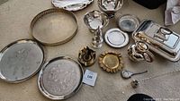 Overview of assorted mixed metal items including trays, bowls, pepper grinder, butter dish and decorative plates displayed on floor.