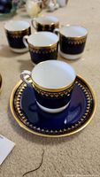 Close-up of a tea cup placed on a matching saucer showing detailed gold pattern on dark blue background.