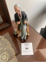 Front view of Royal Doulton The Doctor ceramic figurine showing seated elderly man in black coat holding medical instrument.