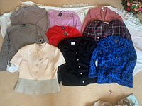 Overview of sweaters, blazers and skirt laid out on floor showing variety of colors and styles.