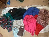 Overview of all clothing items laid on the floor on a light colored rug showing variety of blazers, skirts, tops, and packaged shirts and pants.