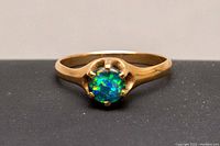 Close-up front view of the gold ring showcasing the round opal gemstone with vibrant blue and green colors.