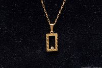 Close-up photo of the rectangular gold pendant featuring a small melee diamond at the bottom center, chain visible.
