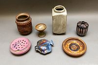 Seven vintage studio pottery pieces in various colors and shapes arranged on a grey surface, showing overall set composition.