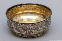 Sterling silver footed bowl showing etched floral and swirl decorations with tarnishing on exterior.