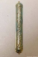 Front side of mezuzah case showing detailed floral repoussé silver design.